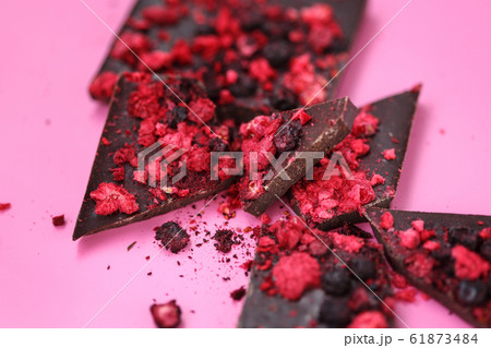 Black chocolate bar broken on pieces with scattered dried red berries and crumbs on pink background Black chocolate bar broken on pieces with scattered dried red berries and crumbs on pink background 61873484