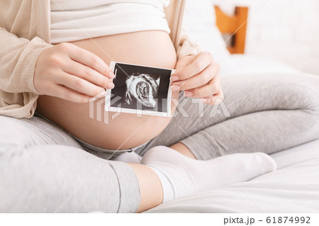 Pregnant woman holding ultrasound picture near belly, closeup Pregnant woman holding ultrasound picture near belly, closeup 61874992