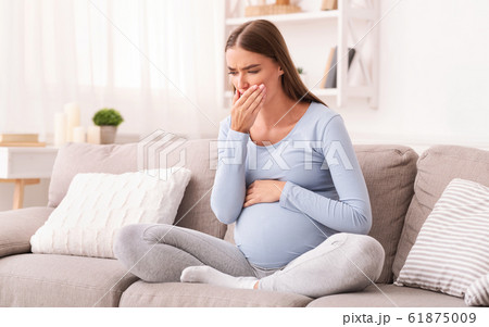 Pregnant Girl Touching Mouth Sitting On Couch Indoor 61875009