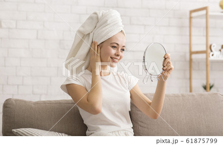 Woman looking at mirror, wearing towel on head after shower Woman looking at mirror, wearing towel on head after shower 61875799