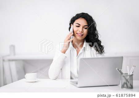 Smiling latin girl talking on the phone at coffee break Smiling latin girl talking on the phone at coffee break 61875894