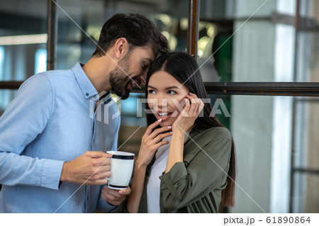 Tall young man having coffee and whispering something in the ear to his colleague 61890864