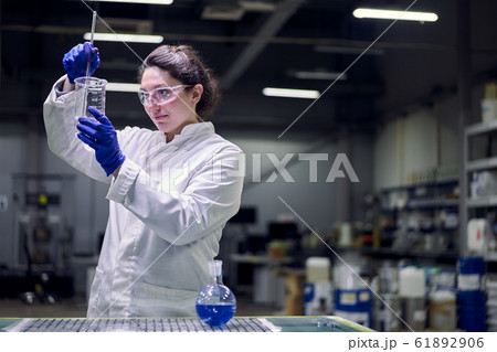 Brunette lab girl in glasses and white coat with experimental glass in her hands conducts experiments Brunette lab girl in glasses and white coat with experimental glass in her hands conducts experiments 61892906