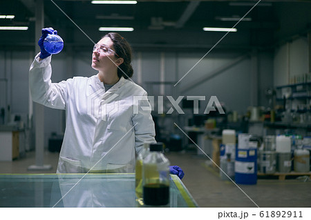 Woman lab assistant with flask in hands with blue liquid on blurred background Woman lab assistant with flask in hands with blue liquid on blurred background 61892911