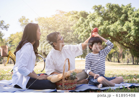 Asian family with son sitting hold apple above his head in the public park. 61895408