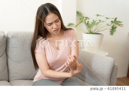 Asian girl having Wrist Pain sitting on sofa at home 61895411