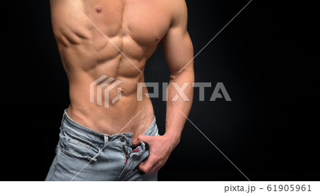 Cropped photo of a sporty man with a muscular body in unbutton shirt and jeans posing in studio. Cropped photo of a sporty man with a muscular body in unbutton shirt and jeans posing in studio. 61905961