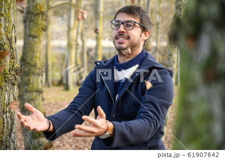 Happy young man playful throwing leaves with open arms dancing under a rain of leaves in autumn park Happy young man playful throwing leaves with open arms dancing under a rain of leaves in autumn park 61907642