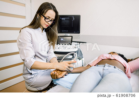 Wrist ultrasound at modern hospital. African woman patient with confident female doctor, having and ultrasound test of the wrist. Wrist ultrasound at modern hospital. African woman patient with confident female doctor, having and ultrasound test of the wrist. 61908706