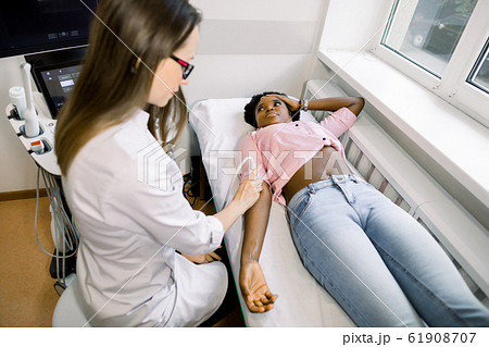 Ultrasound, physiotherapy, rehabilitation concept. Young woman doctor physiotherapist sonographer examining the elbow with an ultrasound scan of her African female patient Ultrasound, physiotherapy, rehabilitation concept. Young woman doctor physiotherapist sonographer examining the elbow with an ultrasound scan of her African female patient 61908707