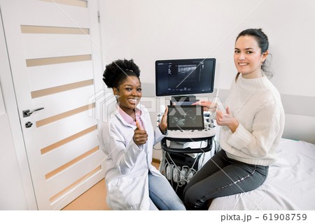 Healthcare, obstetrics and ultrasound concept. African woman doctor and her pregnant patient show thumbs up, smiling and looking at camera, while holding the ultrasound photo of baby on digital tablet 61908759