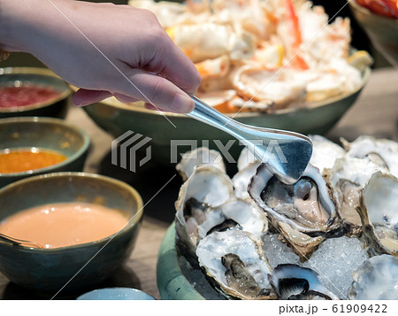 Hand of Asian woman pick a tasty fresh shucked oyster on ice with tongs. 61909422
