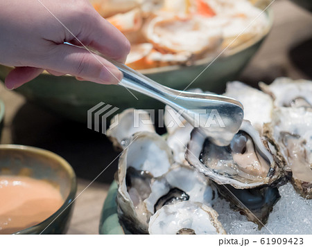 Hand of Asian woman pick a tasty fresh shucked oyster on ice with tongs. Hand of Asian woman pick a tasty fresh shucked oyster on ice with tongs. 61909423