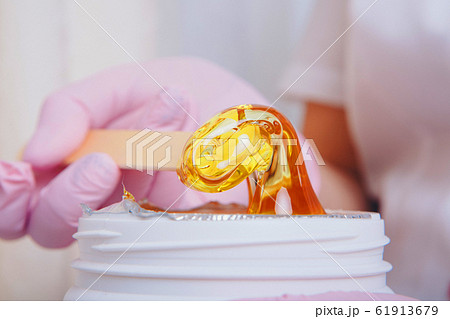 Wax for depilation close-up. girl pulls out cosmetic product from jar. Hand with wooden stick for cosmetic procedures. Sugaring: epilation with liquate sugar at legs 61913679