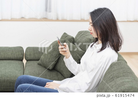 ソファに座って携帯電話を操作する女性 61915474