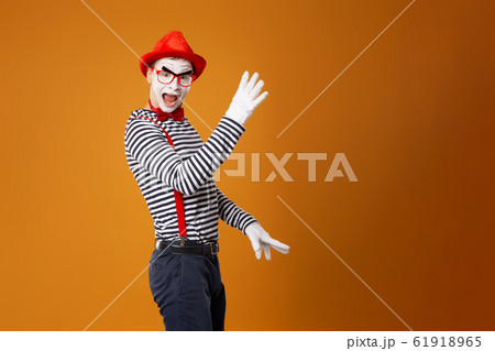 Mime male in white gloves and red hat looking at camera on orange background 61918965
