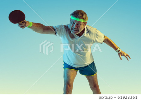 Senior man playing table tennis in sportwear on gradient background and neon light 61923361