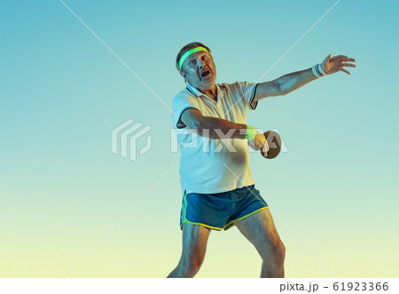 Senior man playing table tennis in sportwear on gradient background and neon light Senior man playing table tennis in sportwear on gradient background and neon light 61923366