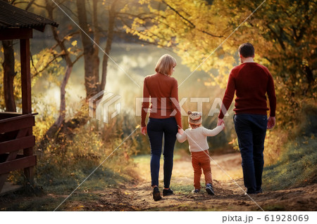Mother father and daughter are walking along the forest path three and around the trees with yellow leaves Mother father and daughter are walking along the forest path three and around the trees with yellow leaves 61928069