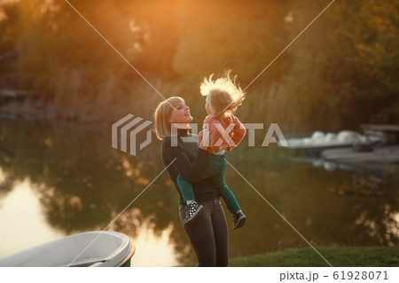 Mom having fun with her daughter near the lake in the autumn on the background of sunset rays Mom having fun with her daughter near the lake in the autumn on the background of sunset rays 61928071