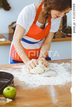 Young brunette woman cooking pizza or handmade pasta in the kitchen. Housewife preparing dough on wooden table. Dieting, food and health concept Young brunette woman cooking pizza or handmade pasta in the kitchen. Housewife preparing dough on wooden table. Dieting, food and health concept 61929469