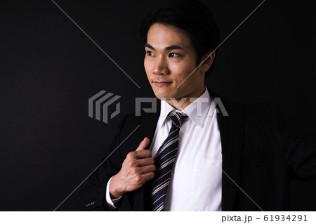 スーツを着るビジネスマン(黒バック、若い男性、上半身 スーツを着るビジネスマン(黒バック、若い男性、上半身 61934291