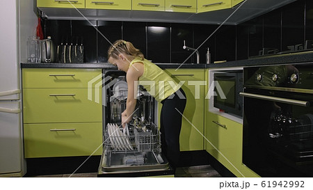 Smart girl learning to use dishwasher. Stylish modern Built In Kitchen Appliances in green black. Child is putting clean dishes. Smart girl learning to use dishwasher. Stylish modern Built In Kitchen Appliances in green black. Child is putting clean dishes. 61942992