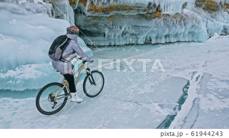 Woman is riding bicycle near the ice grotto. The rock with ice c 61944243