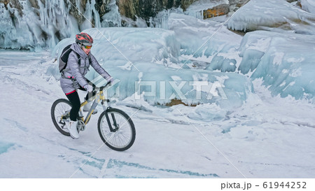 Woman is riding bicycle near the ice grotto. The rock with ice c 61944252