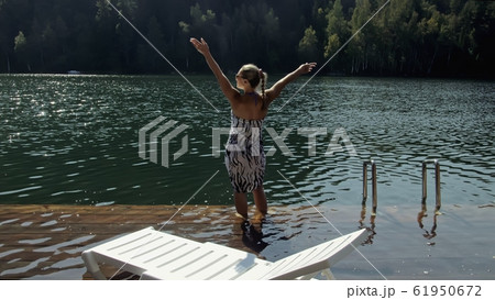 Woman lie on a sunbed in sunglasses and a boho silk shawl. Girl rest on a flood wood underwater pier. The pavement is covered with water in the lake. 61950672
