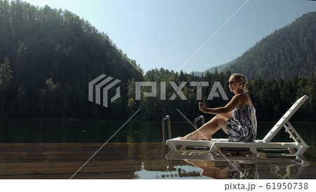 Woman shooting on handheld film gimbal stabilization for smartphone. Girl lie sunbed on pier make selfie. Blogger broadcast video vlogging. 61950738