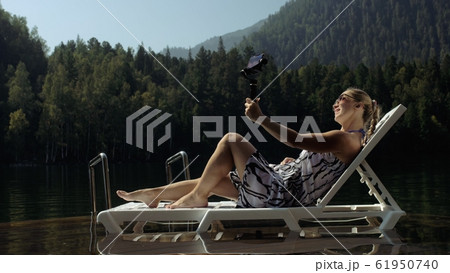 Woman shooting on handheld film gimbal stabilization for smartphone. Girl lie sunbed on pier make selfie. Blogger broadcast video vlogging. 61950740