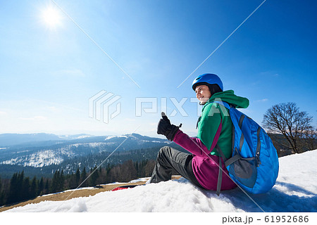 Female snowboarder resting on snowy summit shows thumb-up gesture. Winter sports concept. 61952686