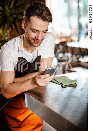 Attractive Caucasian waiter using his cellphone in romantic cafe Attractive Caucasian waiter using his cellphone in romantic cafe 61954723