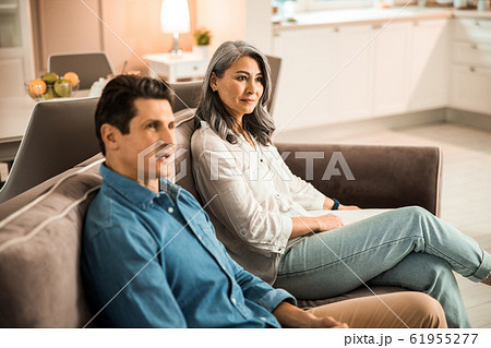 Adult couple sitting on couch and looking away Adult couple sitting on couch and looking away 61955277
