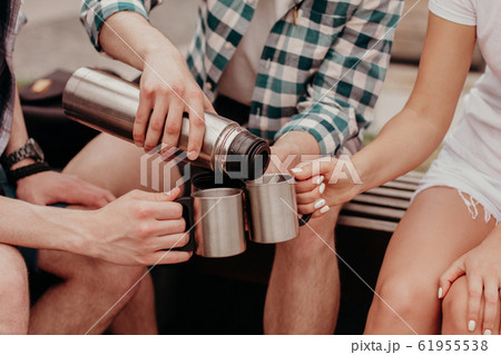 Tea Party On The Street. Three Young Students Pour Tea From A Thermos In Cups Sitting On A Bench. 61955538