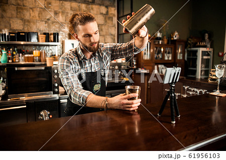 Bearded barman pouring drink from shaker Bearded barman pouring drink from shaker 61956103