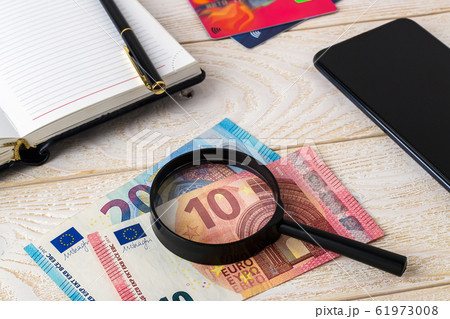 Magnifier on euro banknotes near pen, note book, credit cards and smartphone on a wooden surface. 61973008