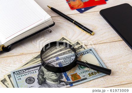 Magnifier on dollar banknotes near pen, note book, credit cards and smartphone on a wooden surface. 61973009