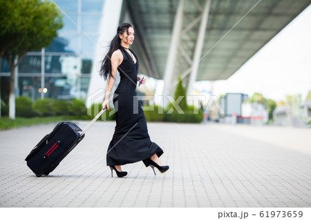 Smiling female passenger proceeding pulling suitcase through airport 61973659