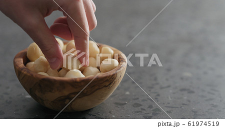 man hand take peeled macadamia nut from olive wood bowl 61974519