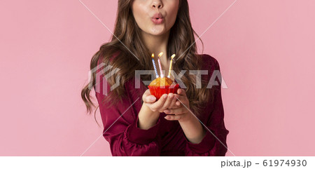 Unrecognizable woman blowing colourful candles on birthday cupcake 61974930