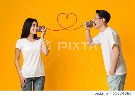 Asian guy telling girlfriend about love, using can phone 61974960
