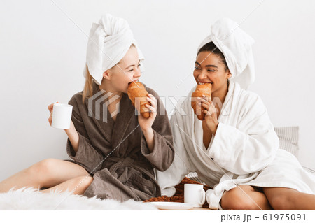 Happy girlfriends in bathrobes and towels on heads having breakfast Happy girlfriends in bathrobes and towels on heads having breakfast 61975091
