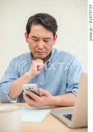 リビングでスマホを見ながら考え込む中高年の男性 61979734