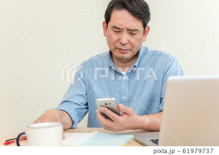 リビングでスマホを見ながら考え込む中高年の男性 リビングでスマホを見ながら考え込む中高年の男性 61979737
