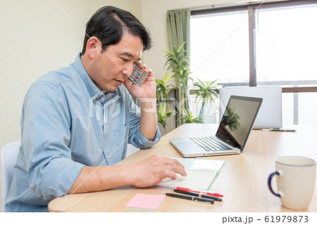 リビングでスマホで電話をしながら資料を見る中年の男性 61979873