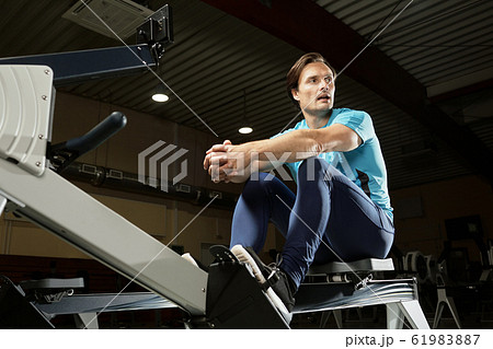 Caucasian male athlete sitting on modern indoor rower and resting after training Caucasian male athlete sitting on modern indoor rower and resting after training 61983887