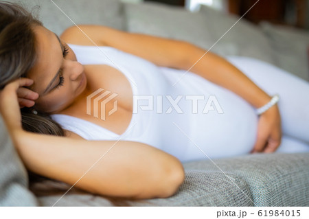 Anxious pregnant woman lying on the sofa with pain Anxious pregnant woman lying on the sofa with pain 61984015