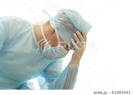 Upset surgeon in sterile gown and surgical mask props his head with hand 61985643